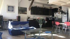 A modern living room with a glass coffee table, a blue sofa, and a kitchen in the background. - Au Cœur de Saint Germain ! 80m2 Confortable, Calme et Lumineux Avec vue (Paris)