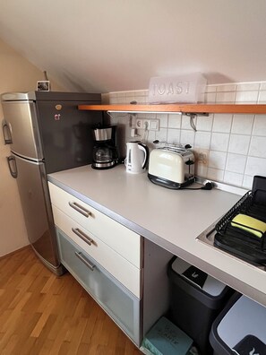 A compact kitchenette with a refrigerator, coffee maker, toaster, and a trash bin. - Peaceful house 4 room house in Maribor - bike friendly (Upravna enota Maribor)