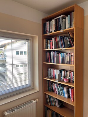 Ein Bücherregal voller Bücher, ein Fenster mit Jalousien und eine Heizung.
