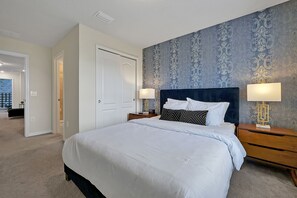 Een slaapkamer met een groot bed, twee nachtkastjes, een deur en behang met een patroon.