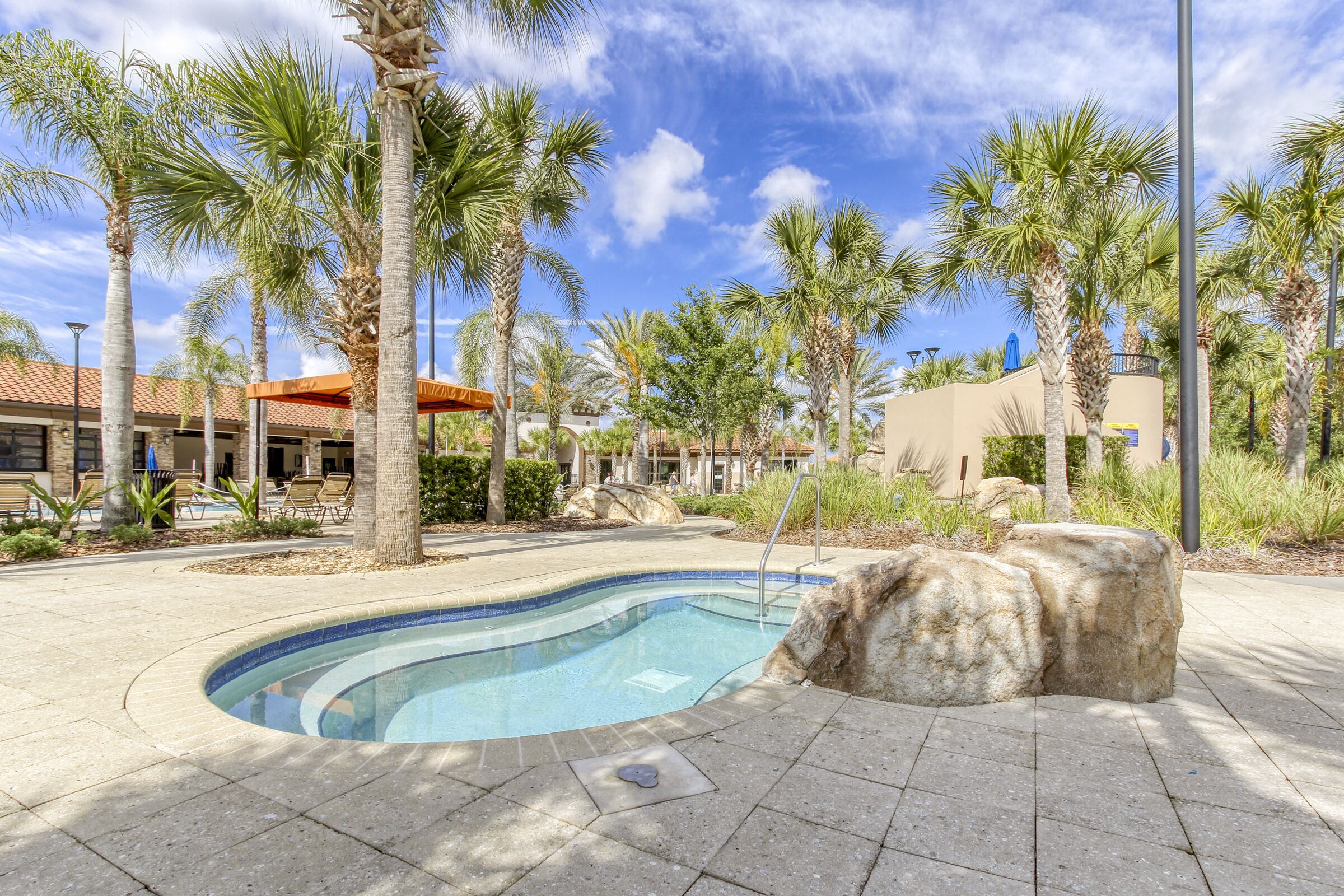 A swimming pool surrounded by palm trees and a building with a red roof.