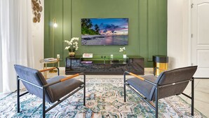 Een moderne woonkamer met een groene accentmuur, een grote televisie, twee fauteuils, een salontafel en een vloerkleed met dessin.