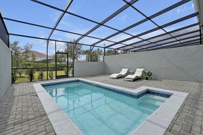 Een zwembad met betegelde rand, omgeven door een terras van bakstenen. Er staan ligstoelen en er is een pergola erboven.