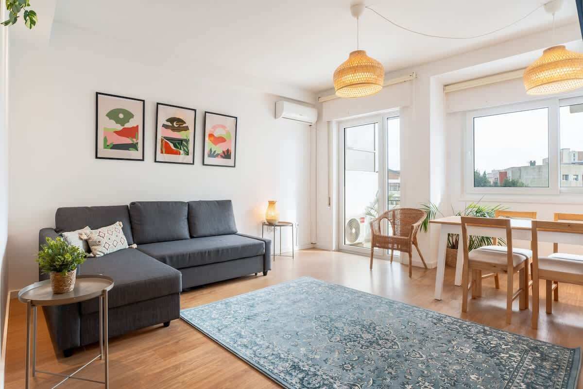 Una sala moderna con un sofá gris, un tapete azul y un comedor con muebles de madera.