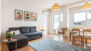 Una sala moderna con un sofá gris, un tapete azul y un comedor con muebles de madera.