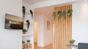 A modern living room with a wooden partition, a mounted TV displaying 'hostwise', and a grey sofa.