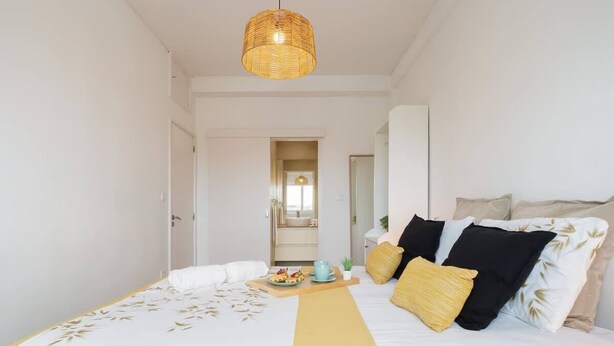 A hotel room with a bed, a bedside table with a tray of food, a hanging light fixture, and a view into the bathroom.