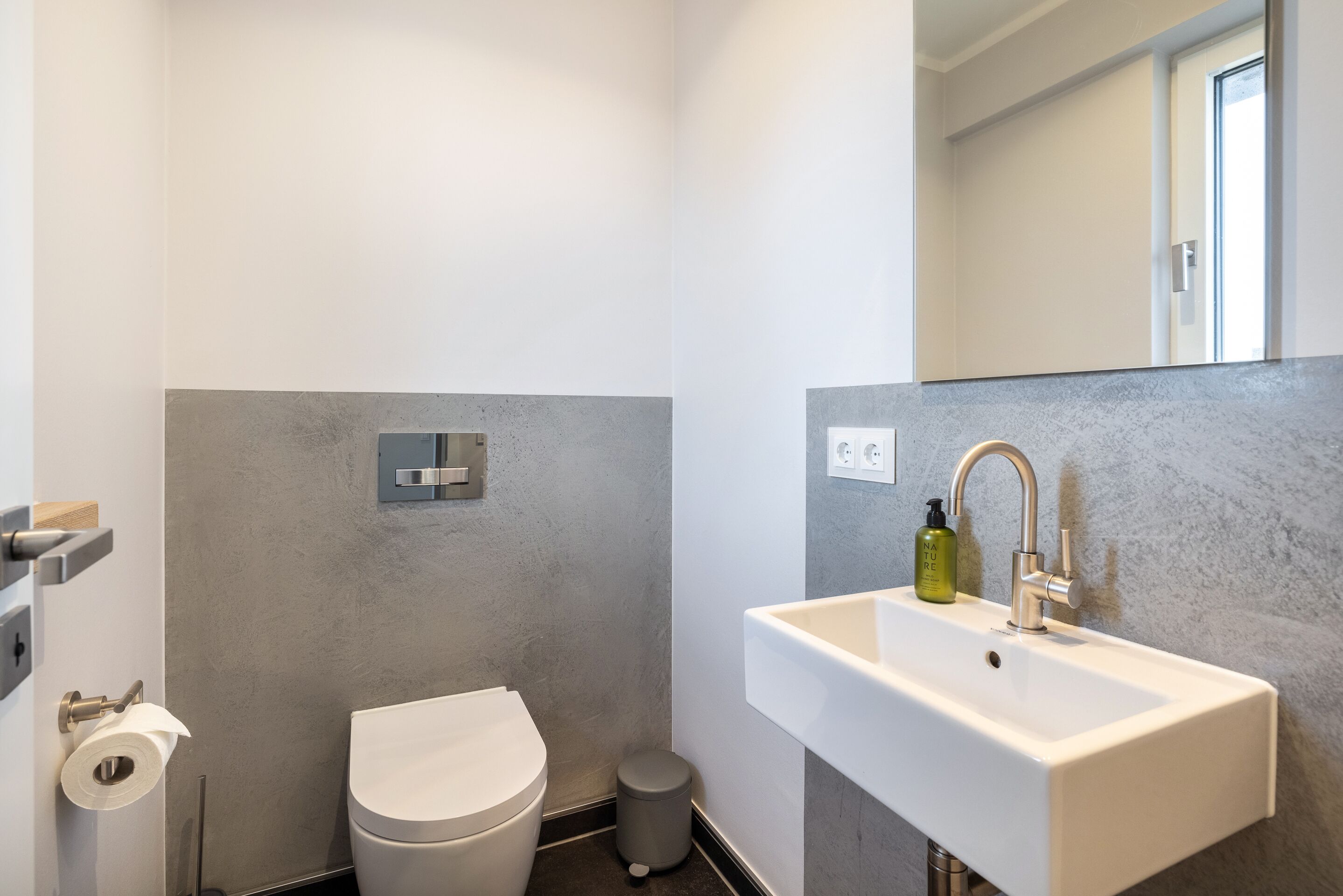 A modern bathroom with a toilet, sink, and mirror.