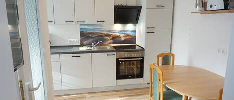 Een compacte keuken met witte kasten, een inbouwoven, een magnetron en een eettafel met stoelen.