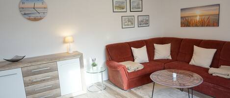A modern living room with a red sofa, a wooden side table, a glass coffee table, and a wall clock.