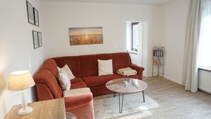 A living room with a red sofa, a round coffee table, a lamp, and a bookshelf. - Ruhige Ferienwohnung in Tönning für bis zu 4 Personen (Tönning)