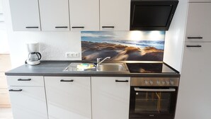 A modern kitchen with white cabinets, a black countertop, a coffee maker, a sink, and a stove. - Ruhige Ferienwohnung in Tönning für bis zu 4 Personen (Tönning)