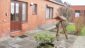 A brick house with a wooden door, windows, and a small garden with a wooden stand and a potted plant. - Ruhige Ferienwohnung in Tönning für bis zu 4 Personen (Tönning)