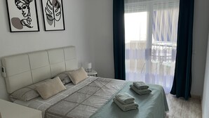 Et soveværelse med en seng, puder, et natbord med lampe og to billeder hængende på væggen.