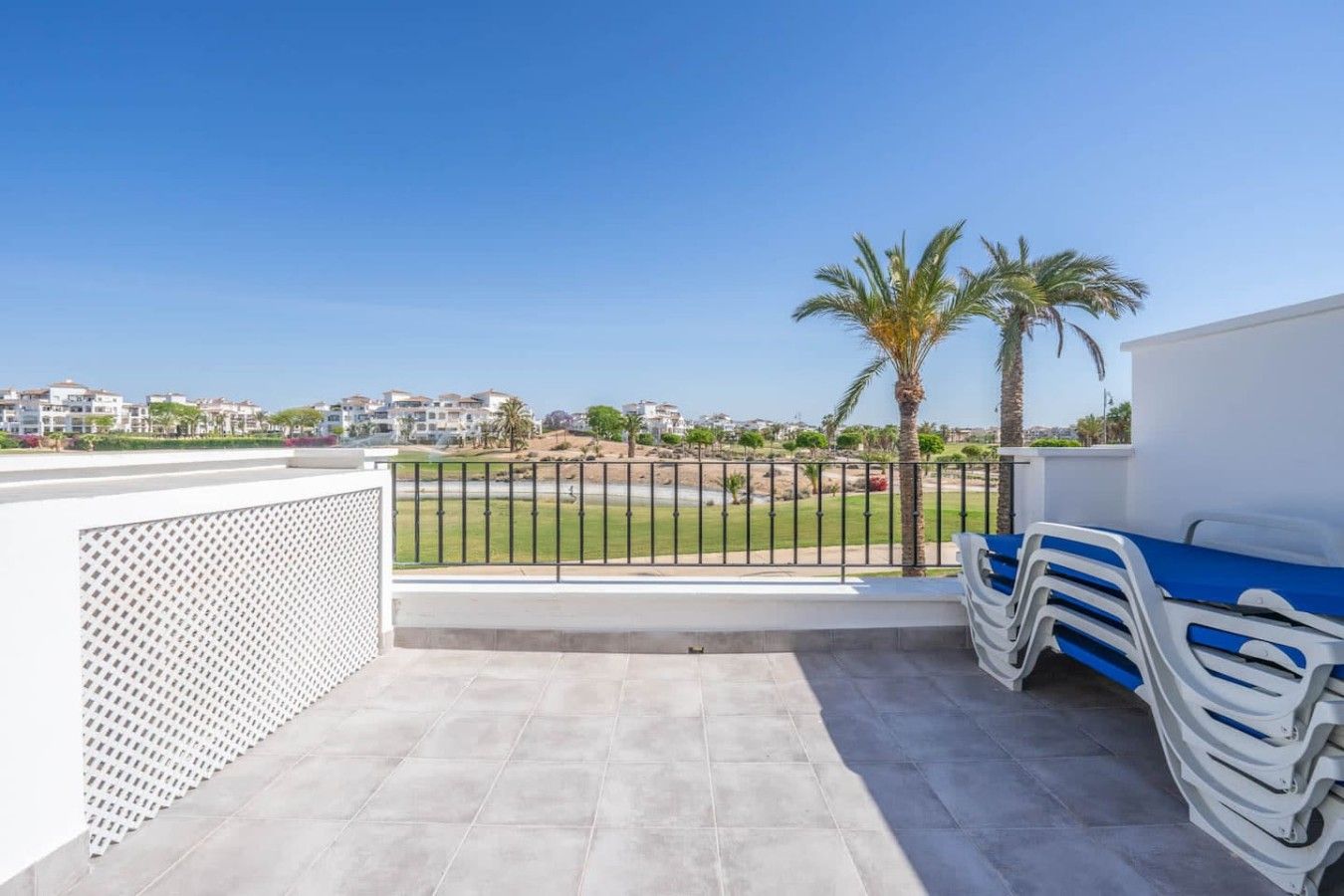 Un balcon donnant sur un terrain de golf, une clôture blanche et une pile de chaises bleues et blanches.