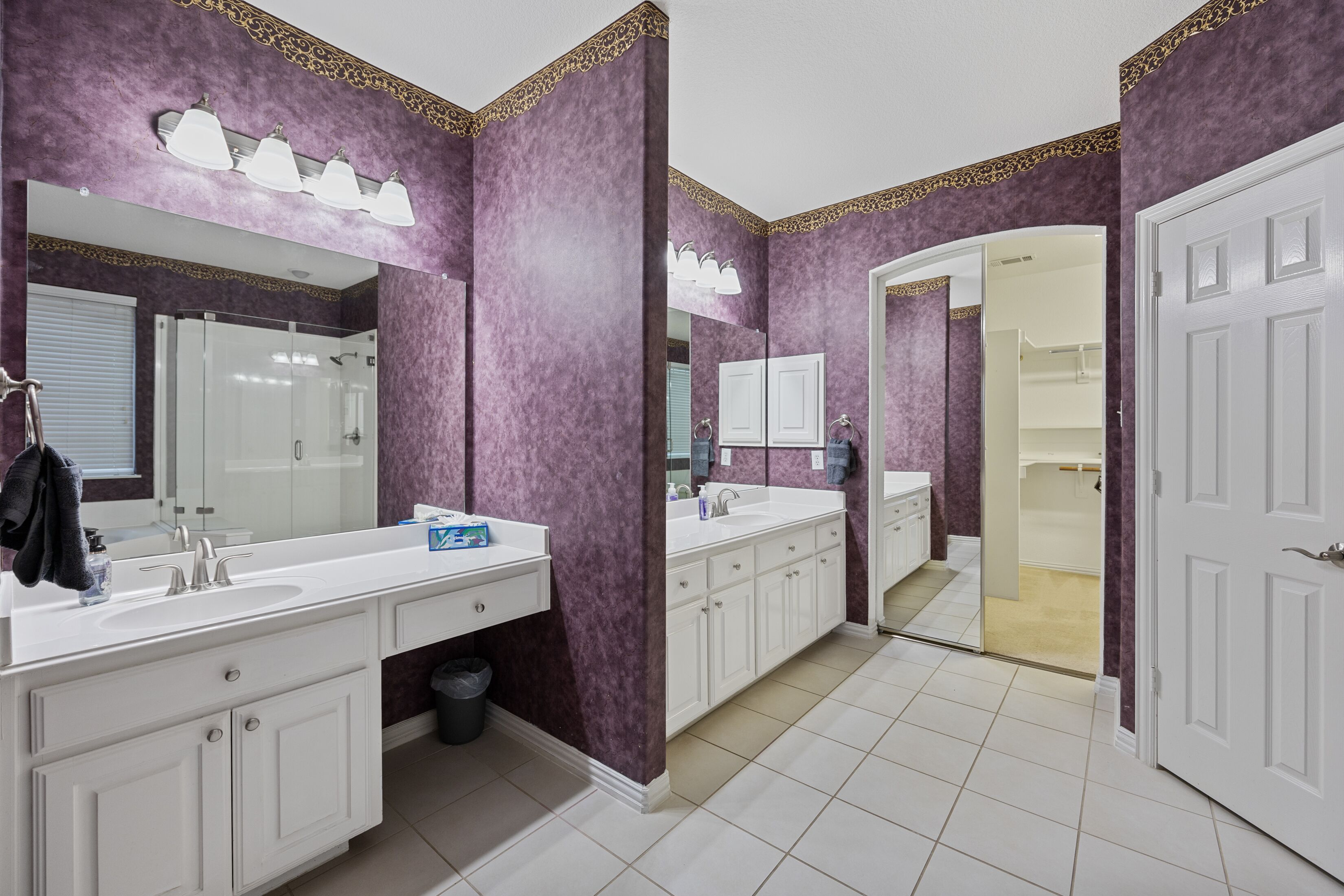 A bathroom with purple walls, white fixtures, and a large mirror.
