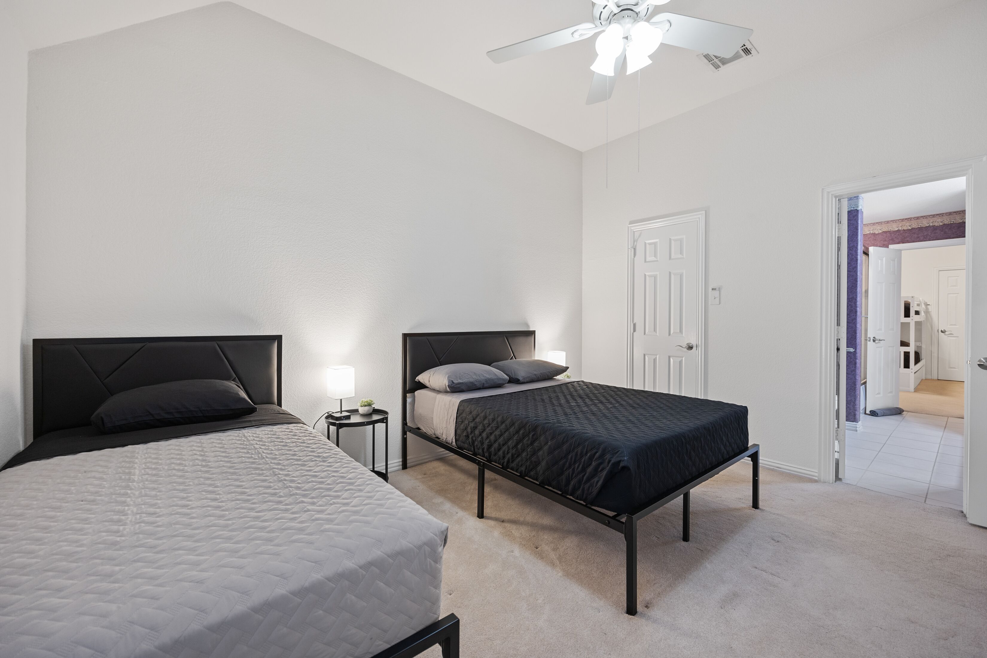 A bedroom with two beds, a ceiling fan, and a door leading to another room.