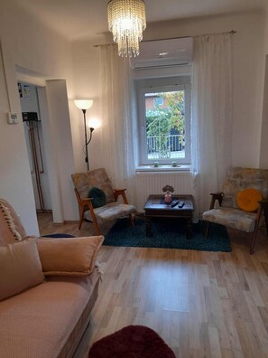 A living room with a chandelier, two armchairs, a sofa, a coffee table, and a view of the outside.