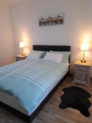 A bed with a headboard, two bedside tables with lamps, a wall with a floral pattern, and a black rug on the floor.