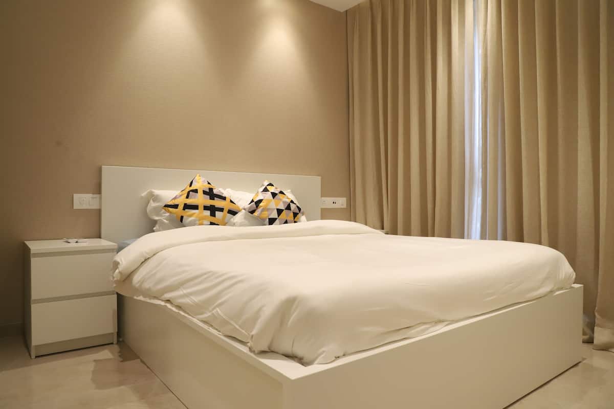 A modern bedroom with a white bed, two pillows with a geometric pattern, a nightstand, and a window with curtains.