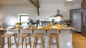 A modern kitchen with a central island, wooden stools, and a brick wall. - The Barn at Plas Ashpool -  a beautiful converted barn sleeping 12 guests (Llandyrnog)