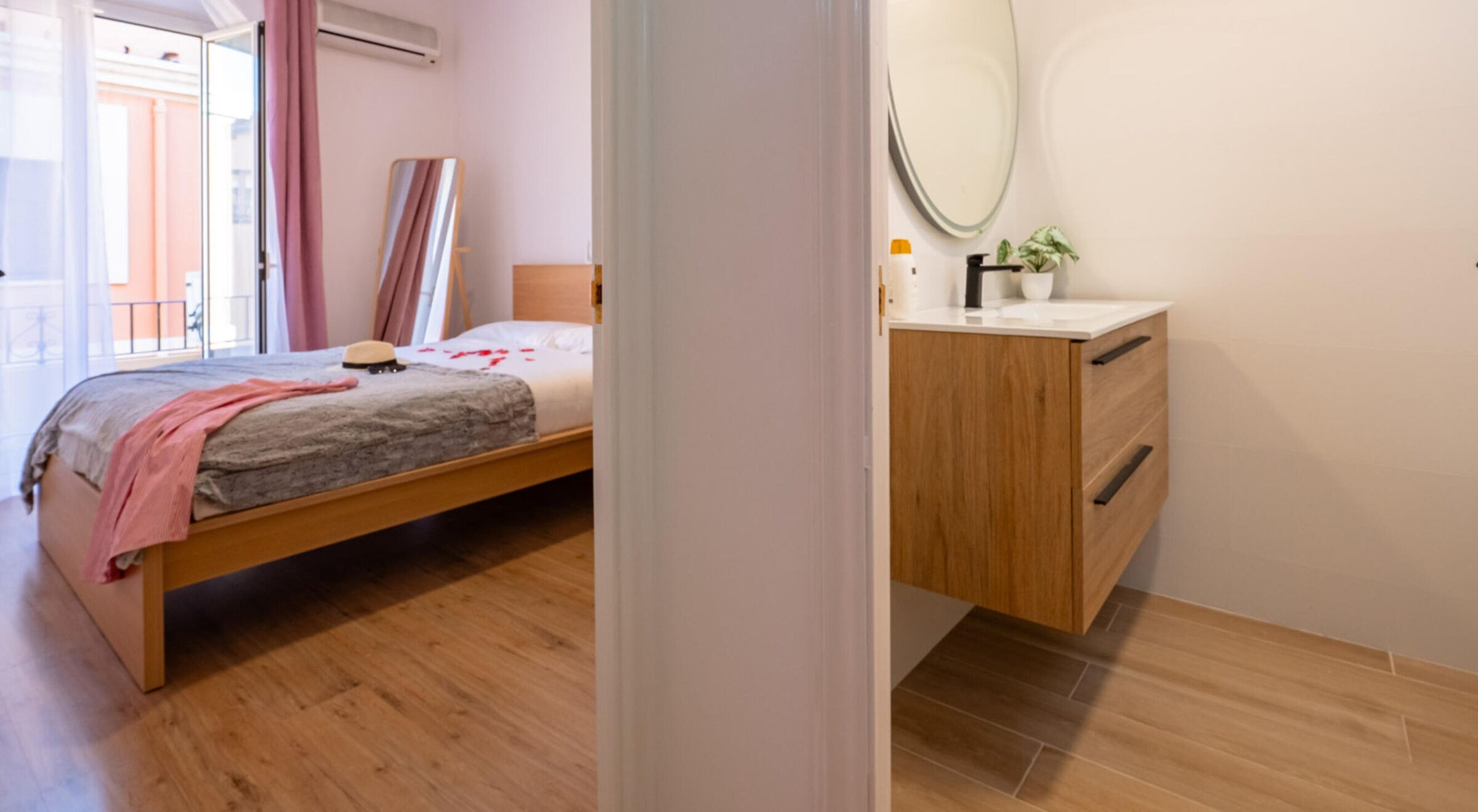 Een slaapkamer met een bed, een nachtkastje, een spiegel en een kleine plant in pot.