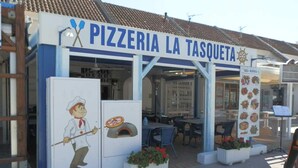 Uma pizzaria com mesas ao ar livre e um quadro de menu exibindo diversos pratos.