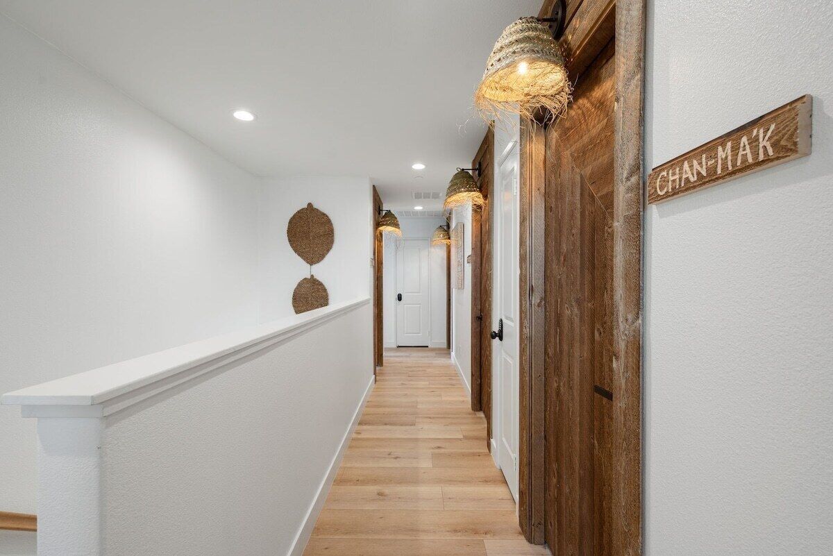 Un pasillo con suelo de madera, paredes blancas y una puerta de madera con un letrero que dice "CHAN-MAK".