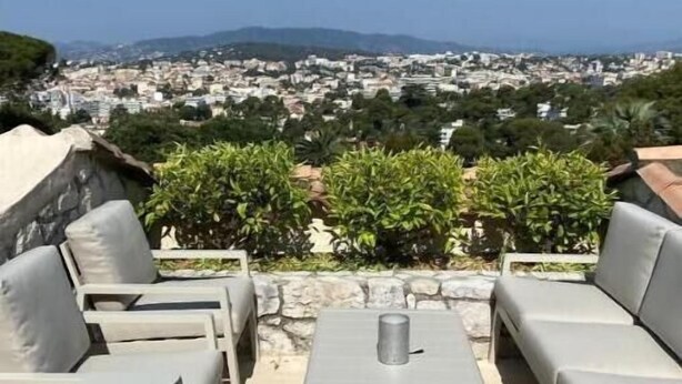 Un espacio al aire libre con mesa y sillas, con vistas a un paisaje urbano con edificios y zonas verdes.