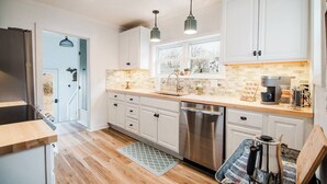 A modern kitchen with white cabinets, a stainless steel dishwasher, and a wooden countertop.