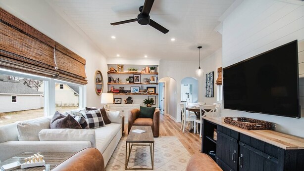 A modern living room with a sofa, armchairs, a coffee table, a TV, and a bookshelf.