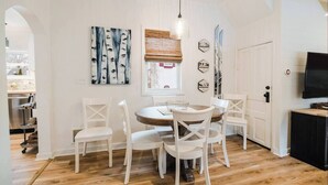 A dining area with a round table, white chairs, a hanging light fixture, and artwork on the walls.