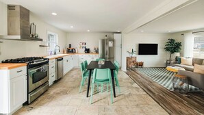 Una cocina moderna con comedor, que incluye una isla central, electrodomésticos de acero inoxidable y sillas color turquesa.