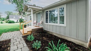 Una casa con porche cubierto, una escalera pequeña y un jardín con plantas.