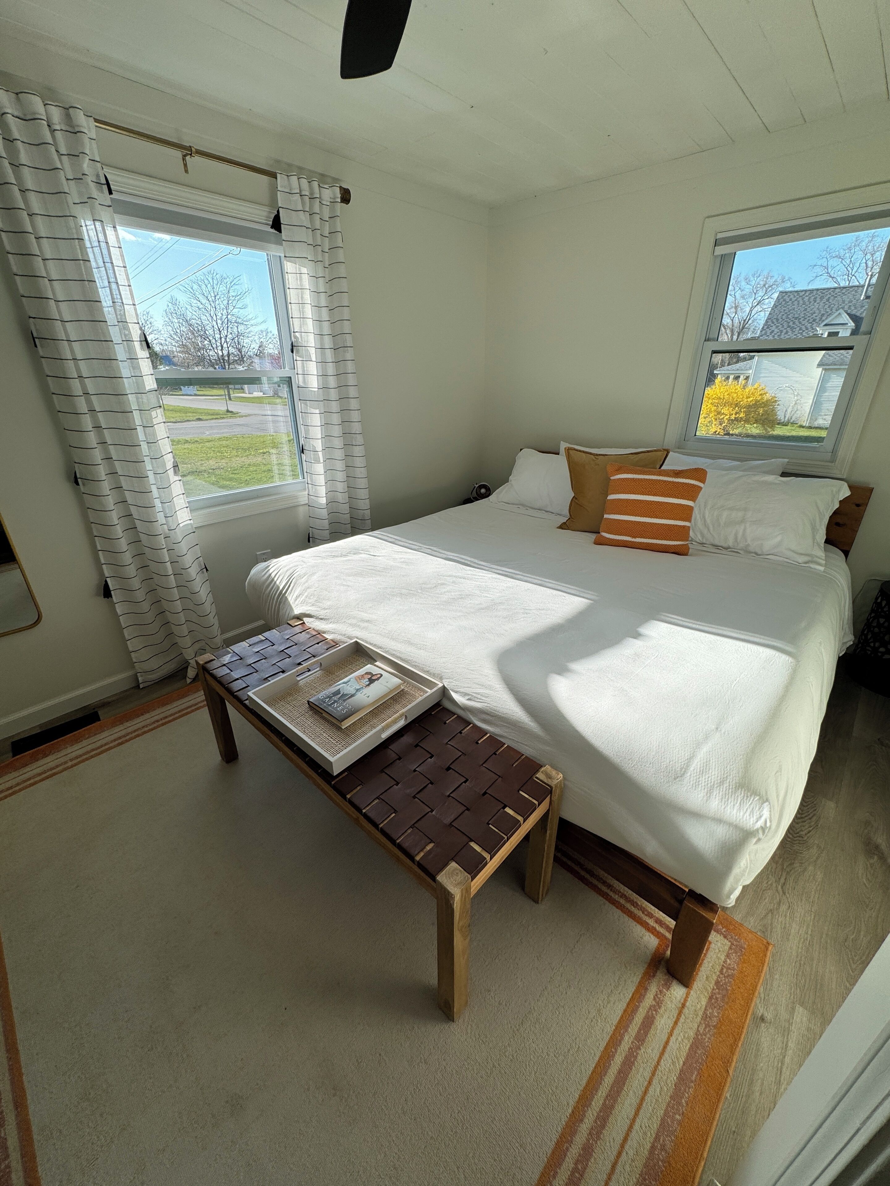A bedroom with a bed, a bedside table with a tray, and a window with curtains.