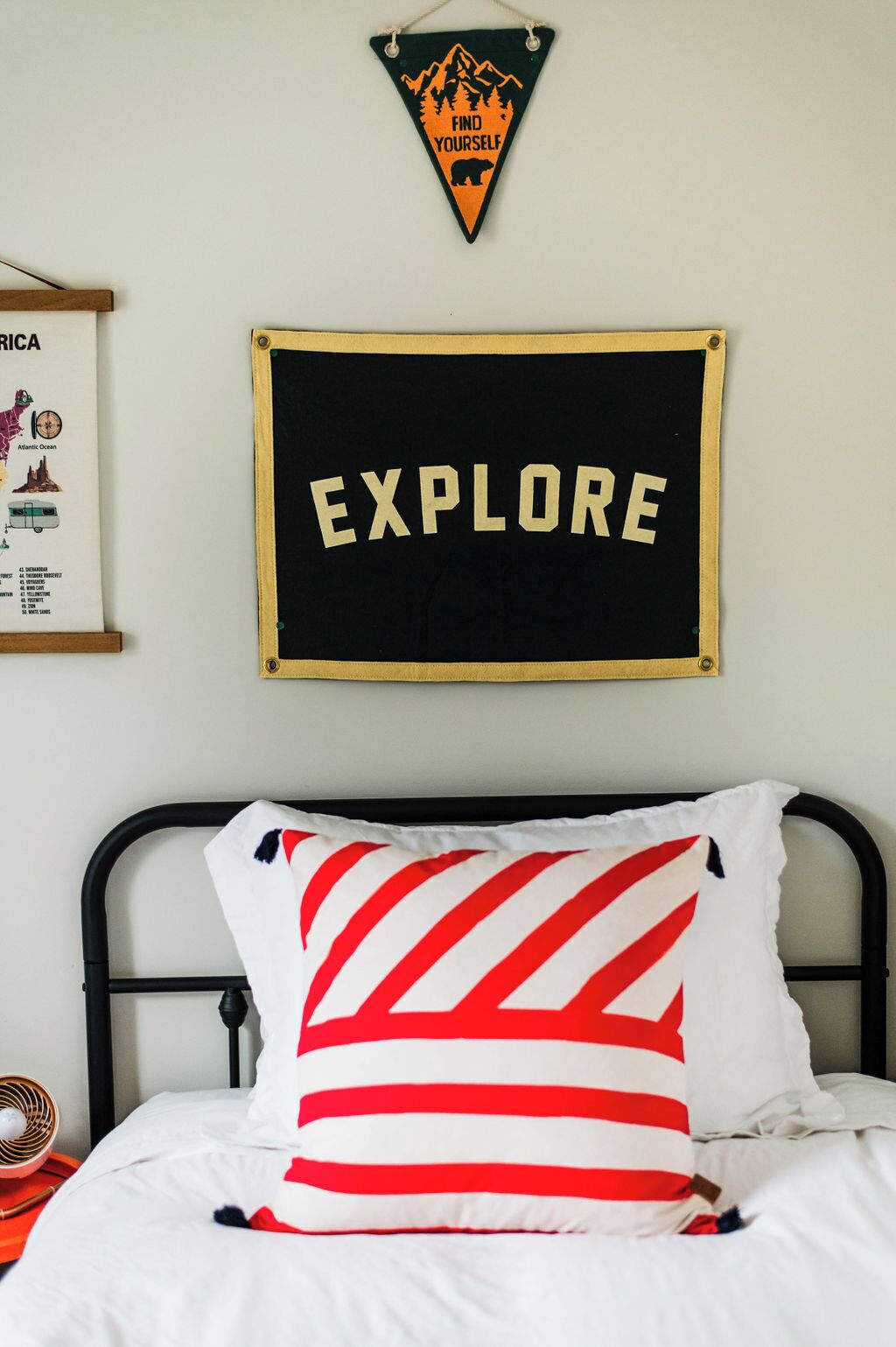 A bed with a striped pillow, a framed map, and a sign that says "EXPLORE" on the wall.