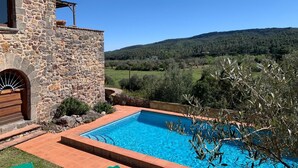 Un bâtiment en pierre doté d’une piscine, entouré d’oliviers et offrant une vue sur un paysage vallonné.