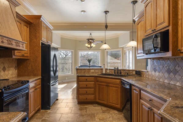 A kitchen with wooden cabinets, a black refrigerator, a stove, and a dishwasher. - Woodland Retreat, Near Branson Fun, FirePit, PS5! (Branson)