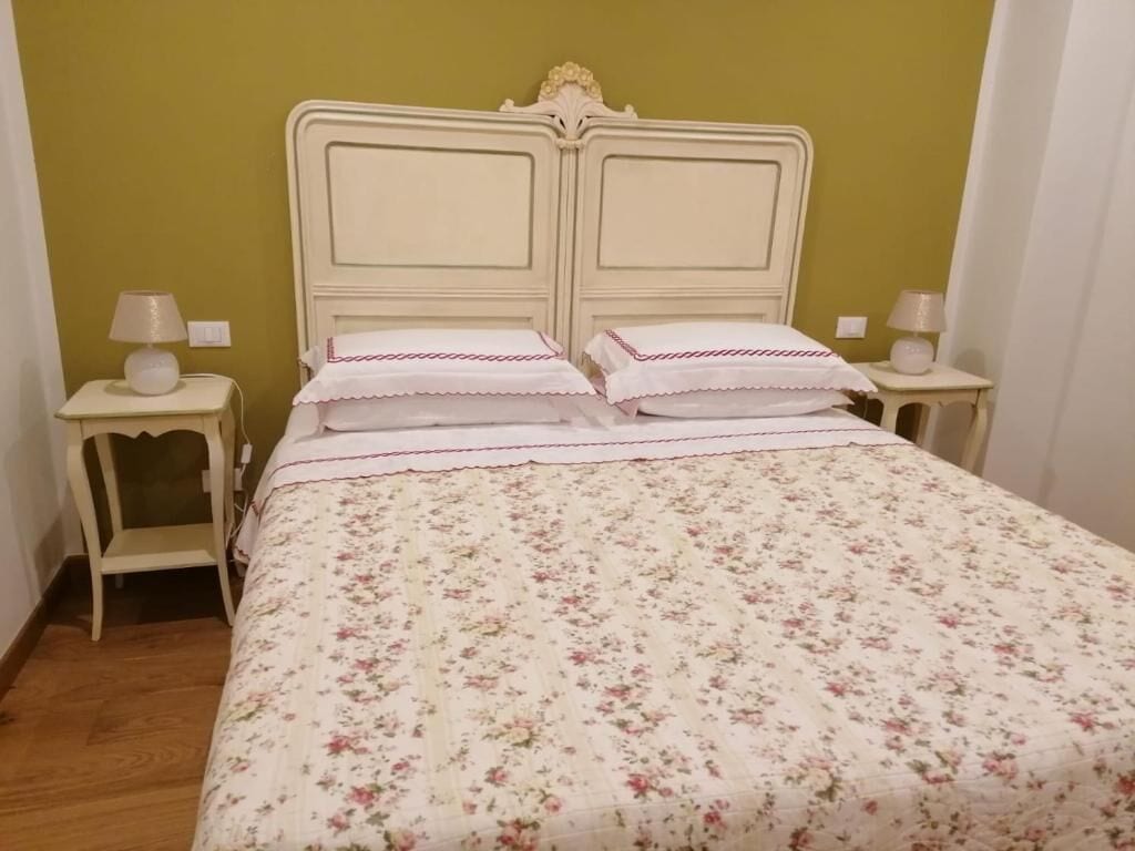 A bed with a floral bedspread and two pillows, flanked by two bedside tables with lamps.
