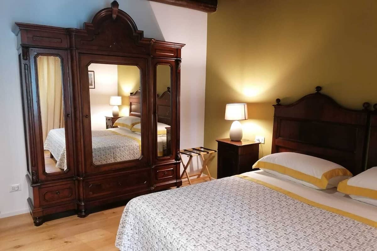Une chambre avec une grande armoire en bois, un lit avec une literie blanche et jaune, et une table de chevet avec une lampe.