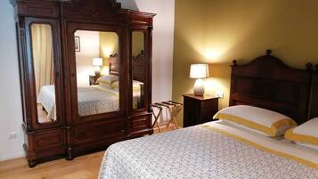 Un dormitorio con un armario grande de madera, una cama con ropa de cama blanca y amarilla, y una mesita de noche con una lámpara.