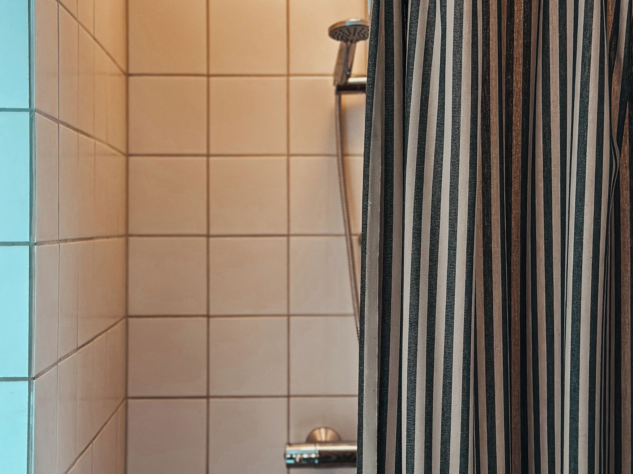 A bathroom with beige tiled walls, a shower curtain with vertical stripes, and a visible showerhead.