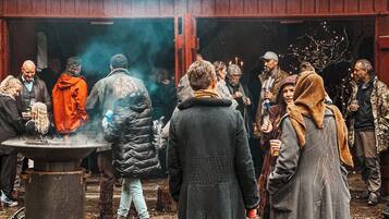 Un grupo de personas reunidas alrededor de un brasero en un entorno al aire libre, con una construcción rústica al fondo.