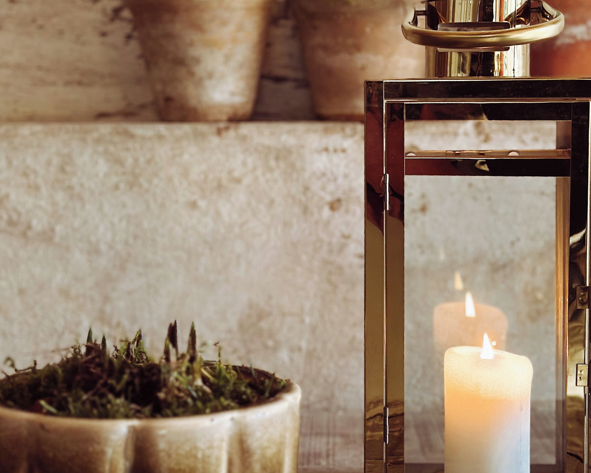 A candle inside a glass lantern with a brass base, placed on a textured surface.