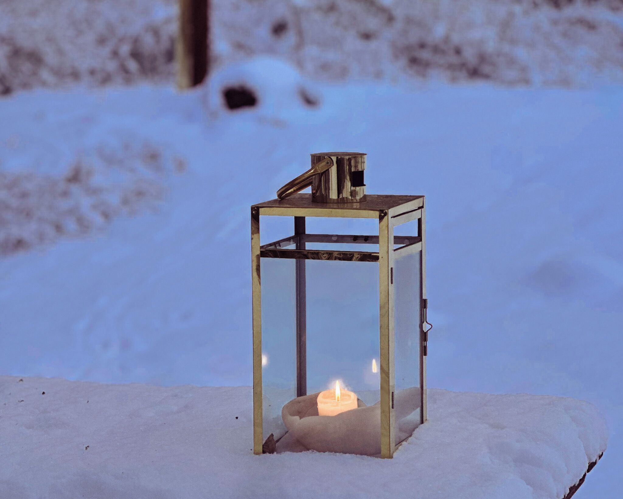 A lantern with a candle inside, placed on a snow-covered surface.
