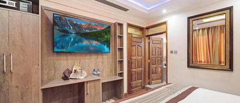 A hotel room with a large bed, wooden wardrobe, a mounted TV, and a mirror.