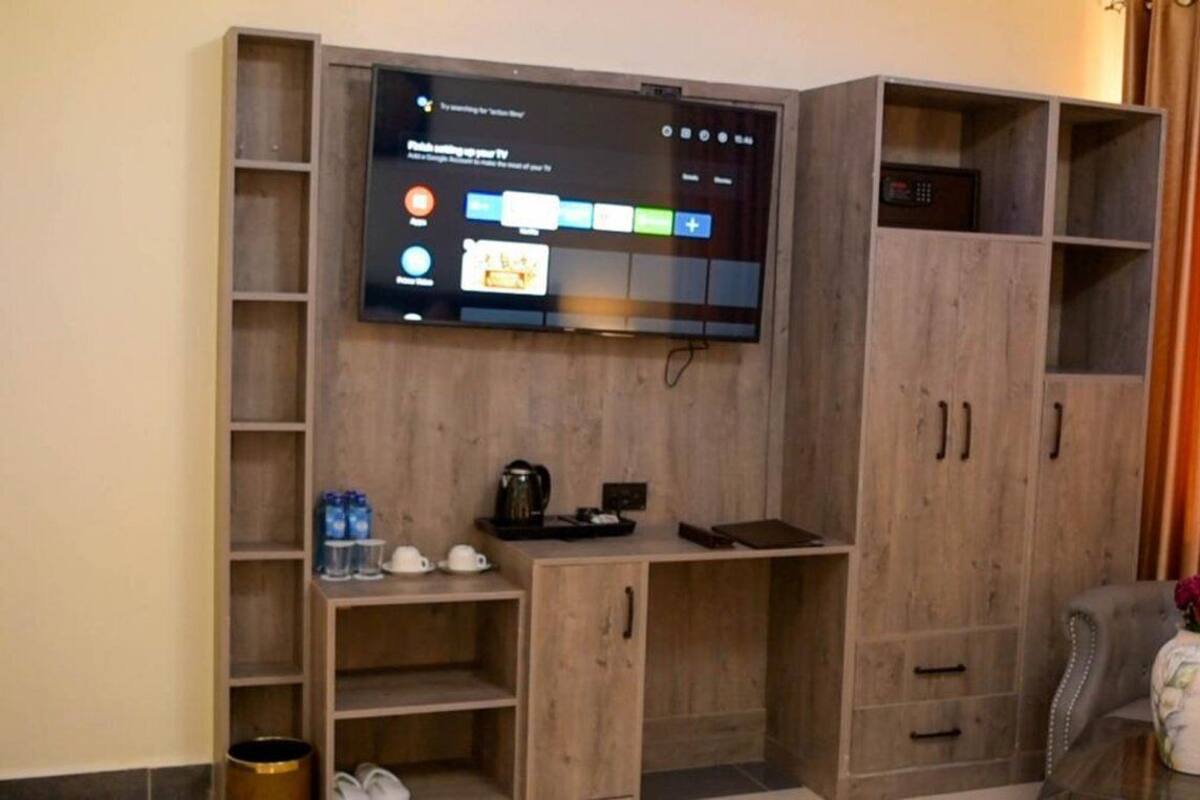 Una sala de estar con un televisor de pantalla plana montado en un mueble de madera, una mesa de centro con un jarrón y un sofá gris.