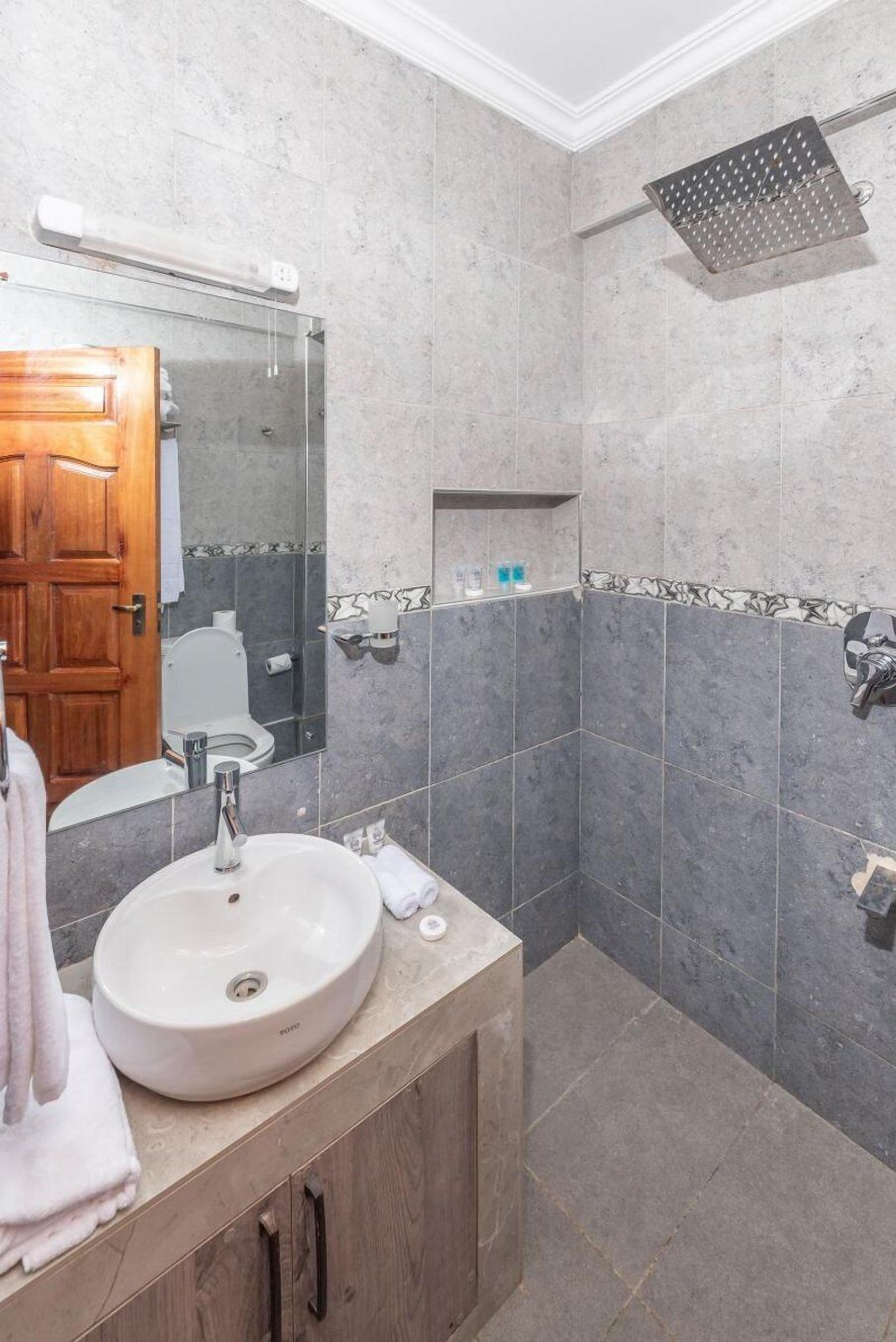 A bathroom with a sink, mirror, shower, and tiled walls.
