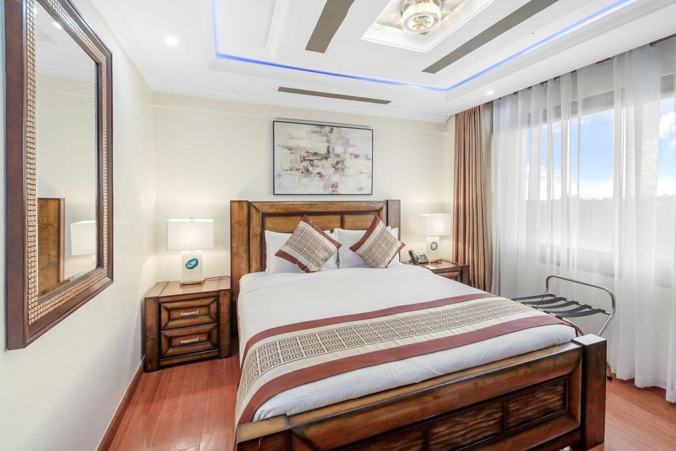 A hotel room with a large bed, bedside tables, a ceiling light, a painting, and a window with curtains.