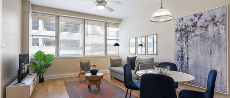 A modern living room with a sofa, dining table, chairs, a ceiling fan, and a large abstract painting.
